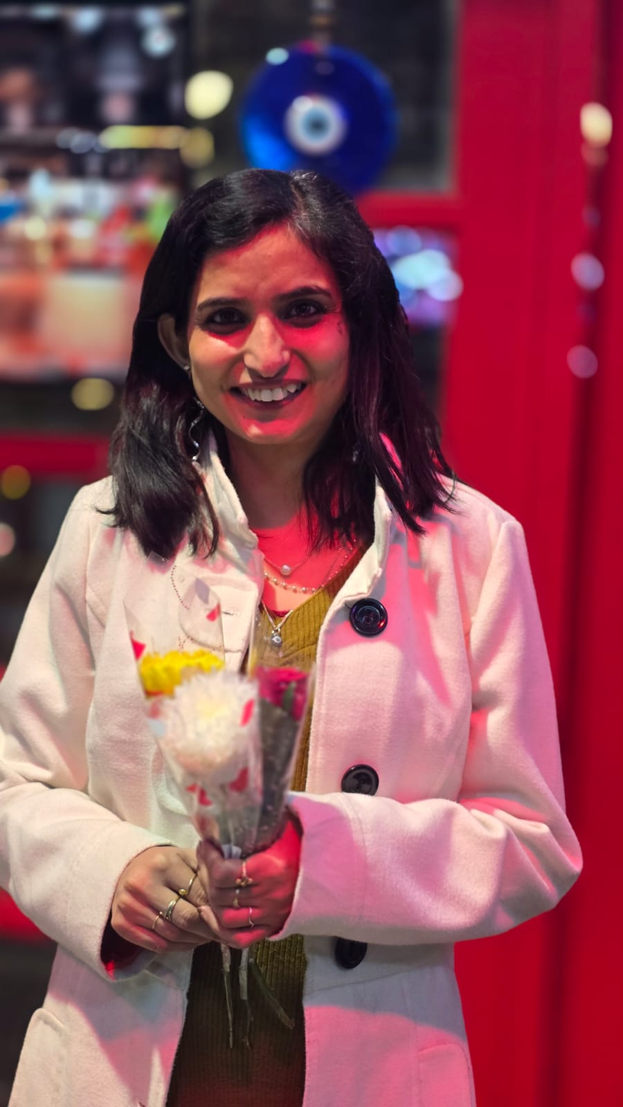 Evening out — white coat, holding flowers, bathed in rose-pink light