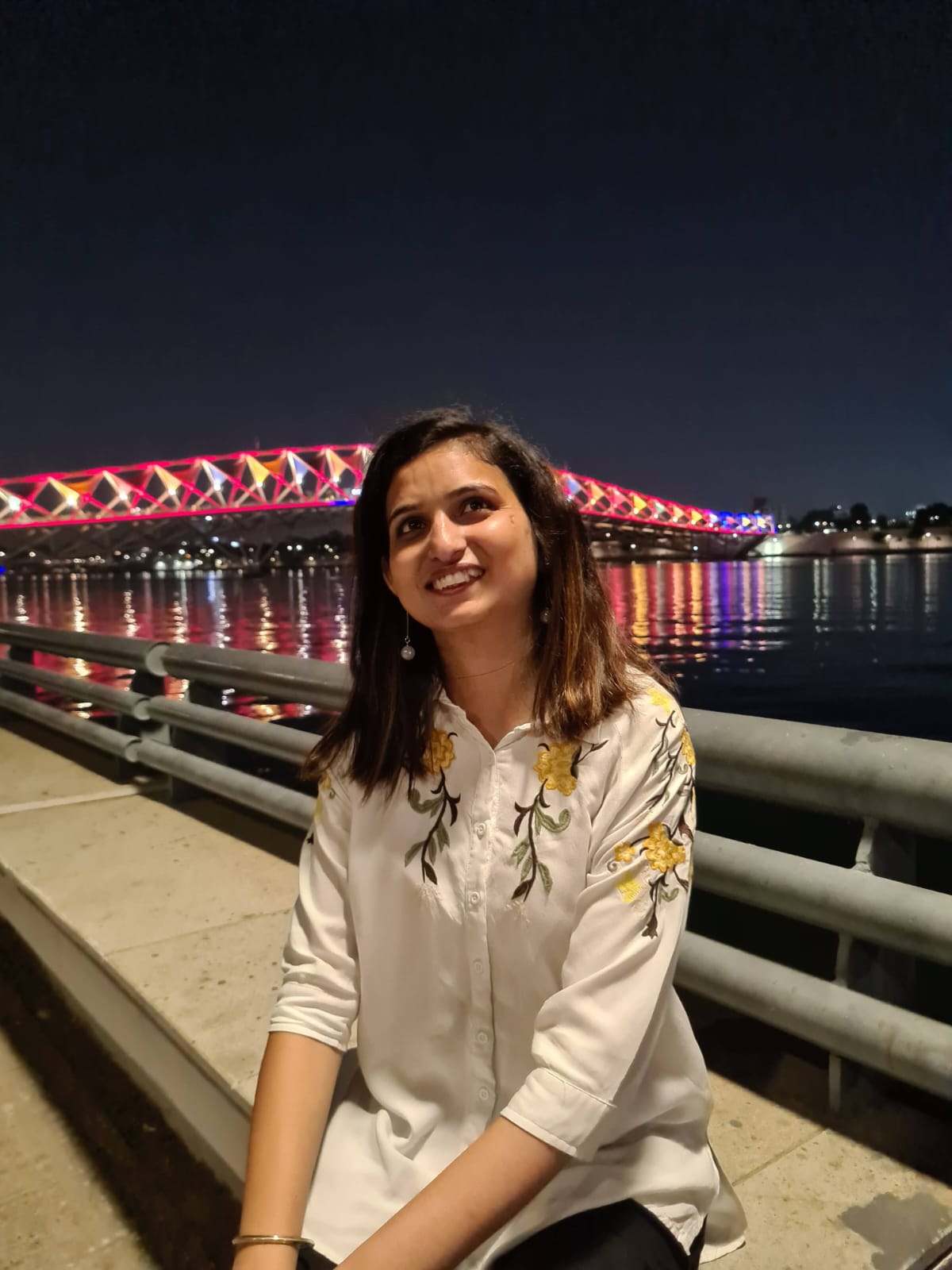 Candid — seated on steps, looking up, bridge lights reflecting on water behind