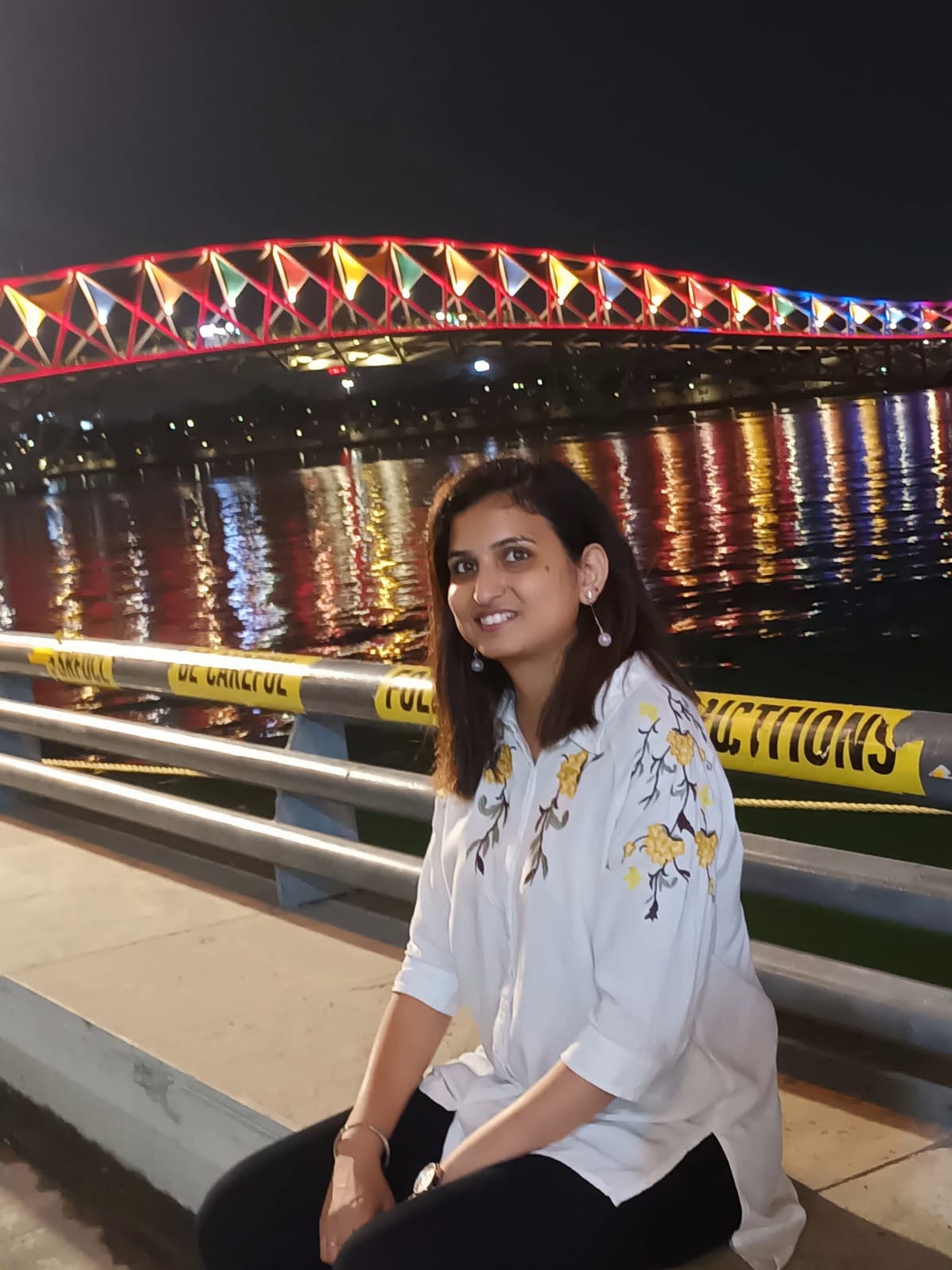Candid — seated at riverside, colourful bridge lights in background